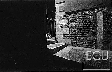 Black and white photo of an entrance to a Venetian bridge in Venice at night with space disappearing into darkness